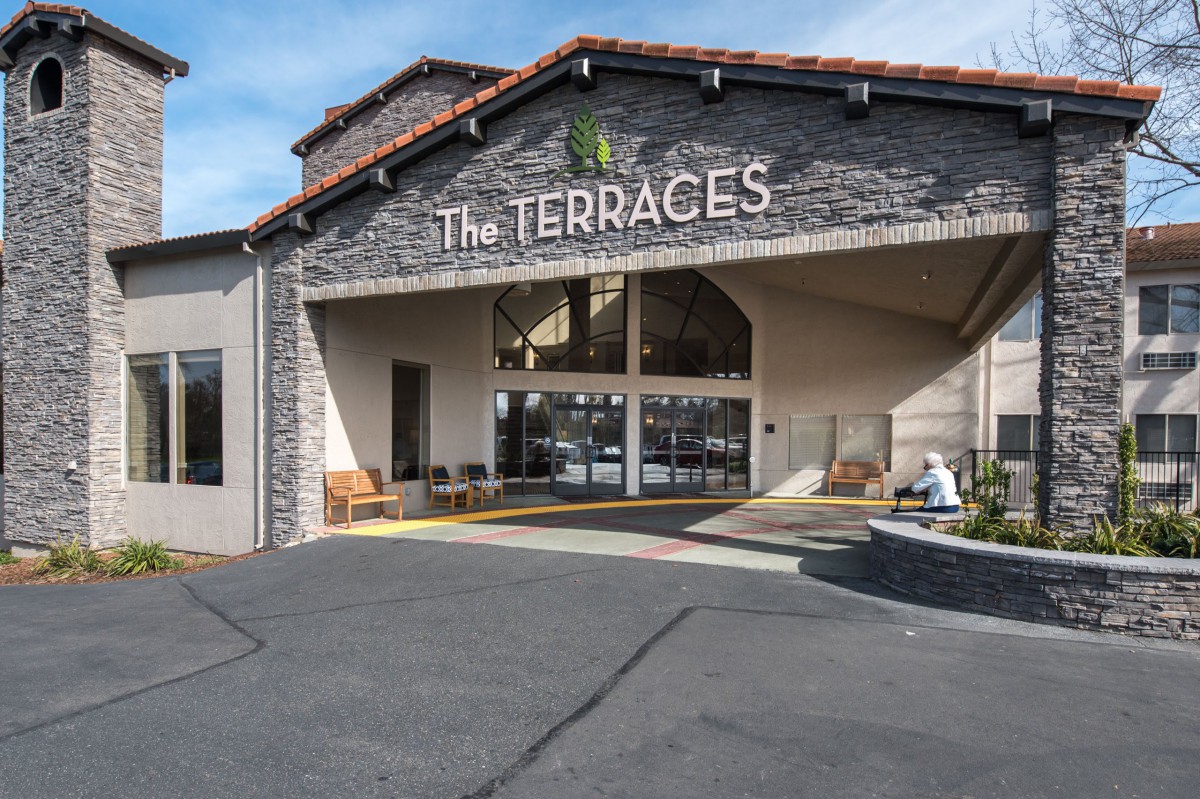 Entrance of a building labeled 'The Terraces' with a stone facade and outdoor seating.