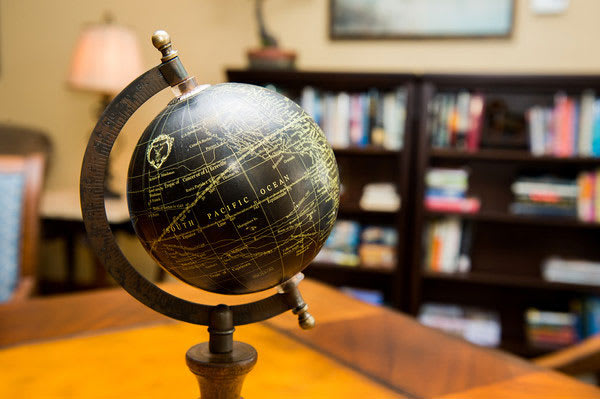 A decorative globe sits prominently on a desk in front of a well-stocked bookshelf, suggesting a scholarly or office environment.