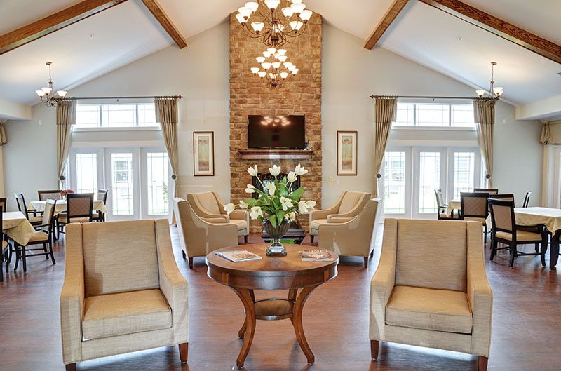 A spacious, elegantly designed living room featuring a high ceiling with wooden beams and a central stone fireplace.