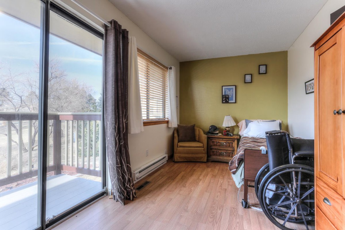 A bedroom featuring a wheelchair, with access to a balcony through sliding glass doors.