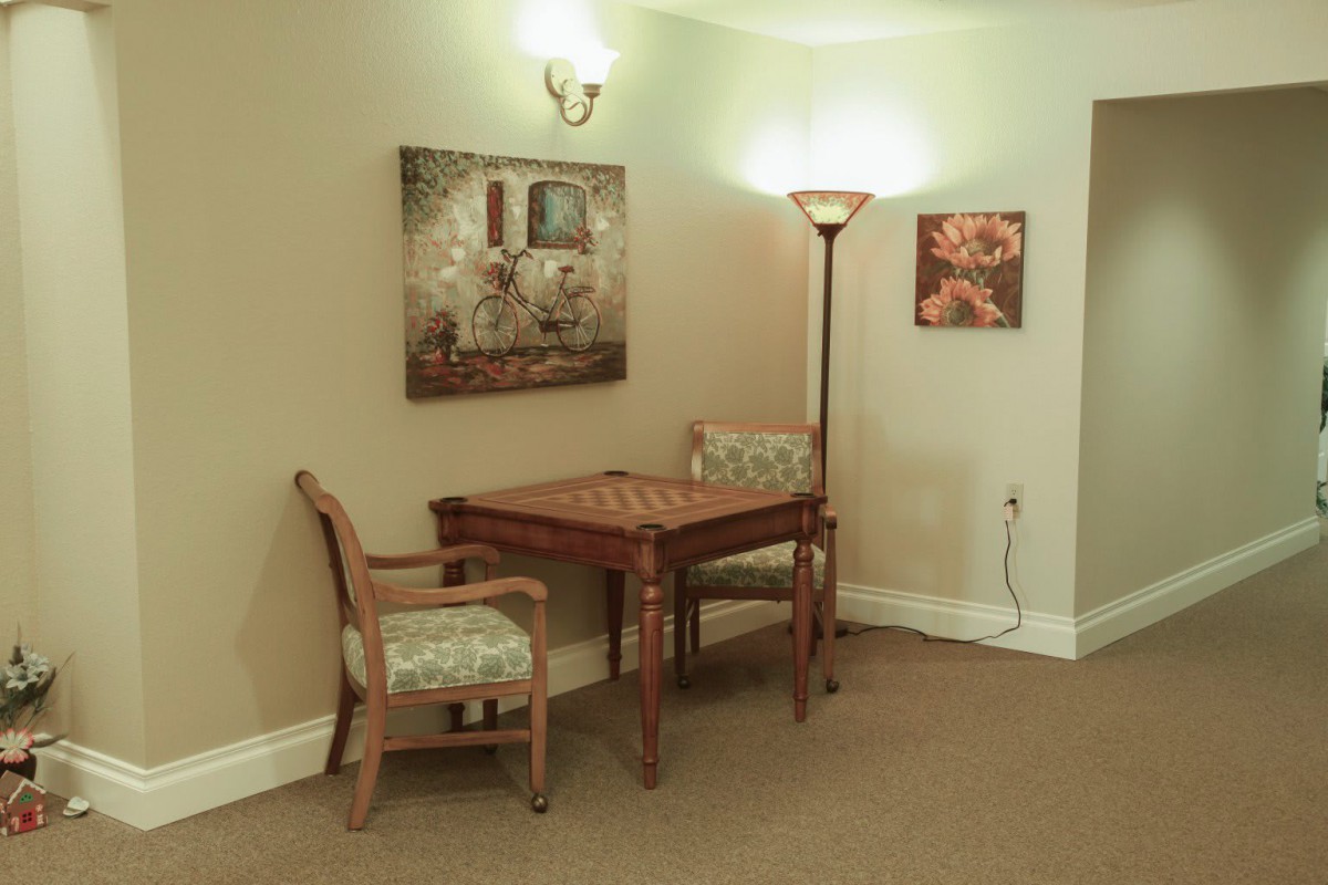 A cozy corner with a wooden table, matching chairs, a floor lamp, and framed artwork on the walls.