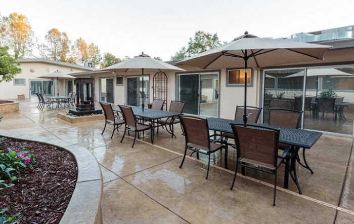A residential patio with multiple tables and chairs under umbrellas, set on a wet pavement.