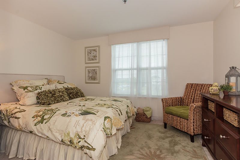A cozy bedroom with a floral-patterned bedspread and a striped armchair by the window.
