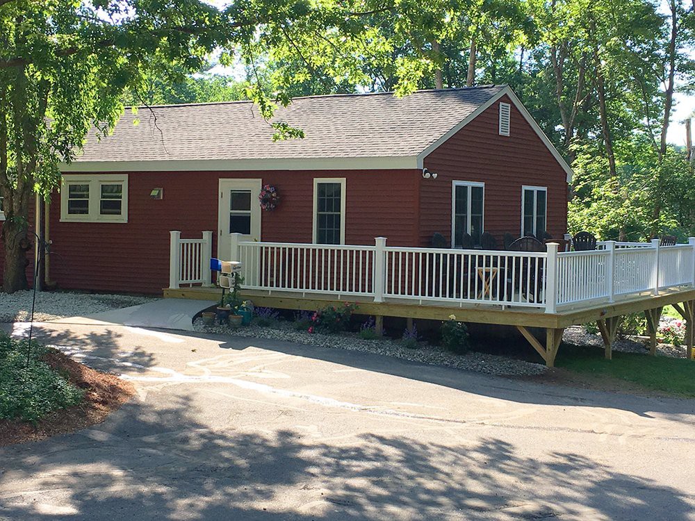 A red ranch-style house with a white porch surrounded by trees on a sunny day.