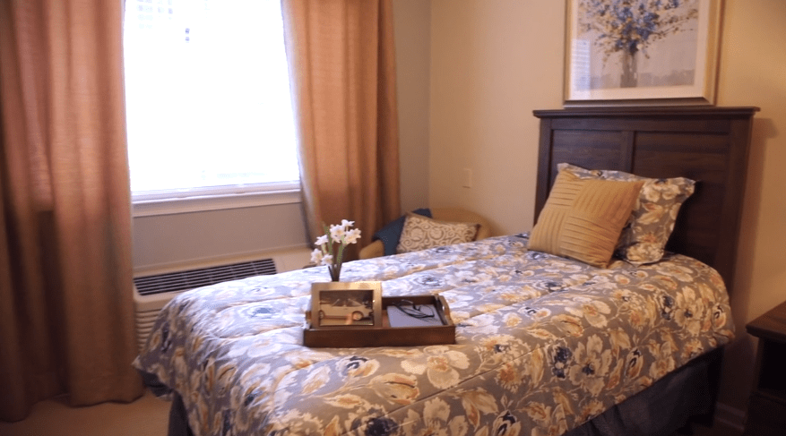 A cozy bedroom with a floral quilt on the bed and a tray holding books and flowers.