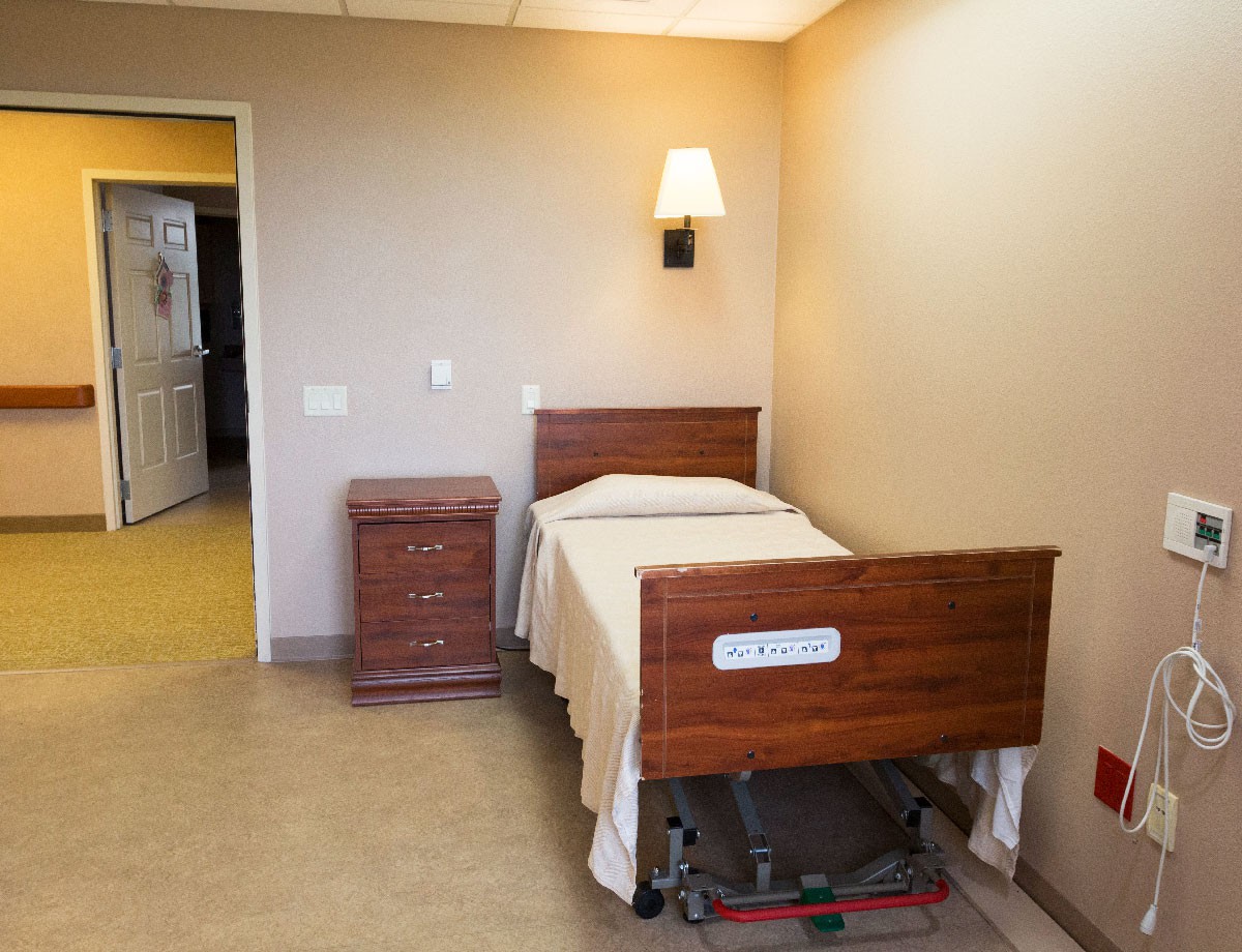 A simple hospital room with a single bed and a nightstand.