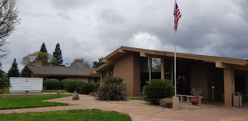 A modern building with landscaped surroundings and an American flag, set against a cloudy sky.