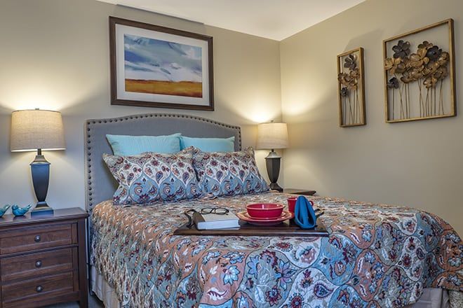 A cozy bedroom featuring patterned bedding, wall art, and a bedside lamp.