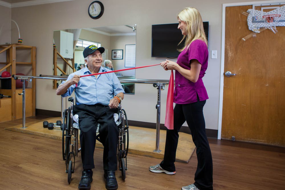A therapist assists a man in a wheelchair during a rehabilitation exercise session.