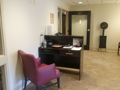 A cozy office waiting area featuring a red chair and a desk.