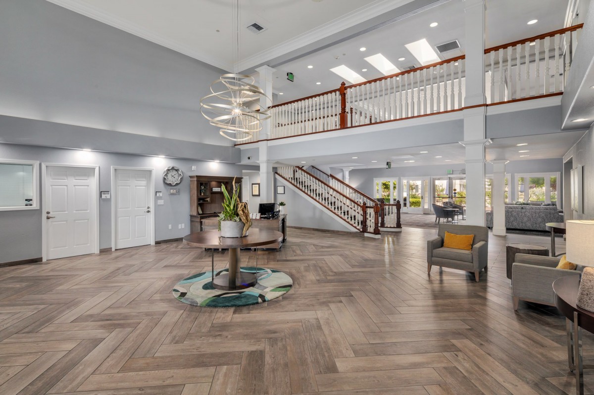 A spacious and modern lobby area featuring a stylish chandelier, wooden flooring, and an elegant staircase.