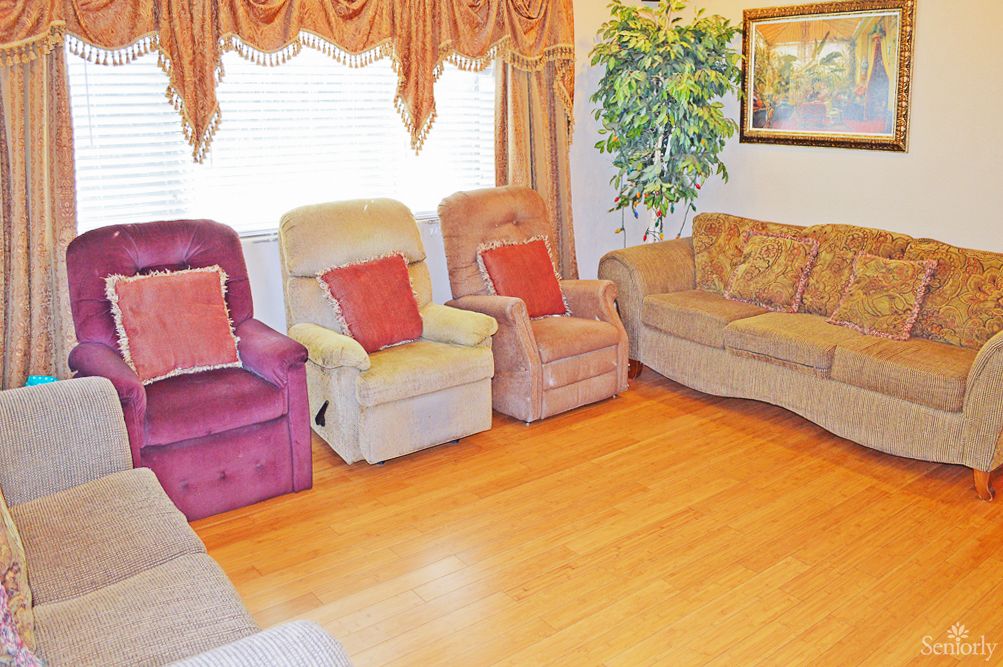 A cozy living room with a sofa, reclining chairs, and hardwood flooring.