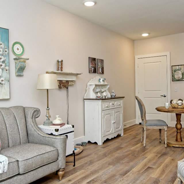 A cozy vintage-style living room featuring a gray couch, decorative art, and wooden flooring.