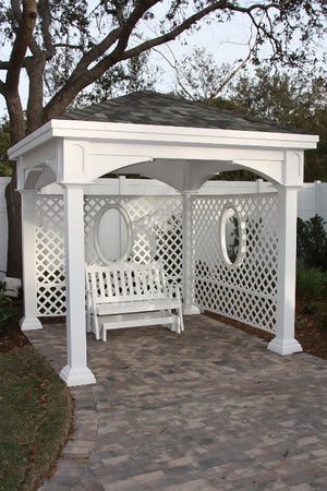 A white gazebo with lattice sides, featuring a hanging swing on a patio.