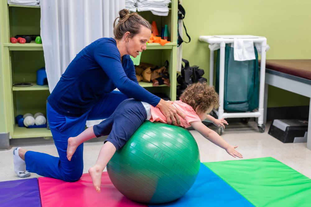 A therapist helps a child with exercises using a fitness ball for physical therapy.