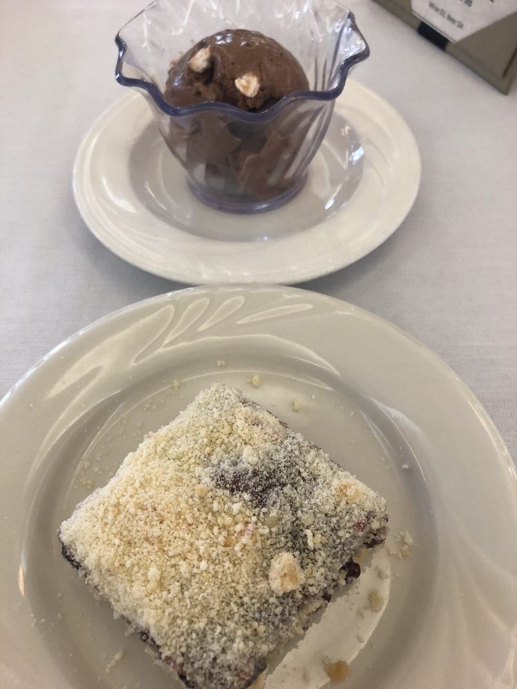 A plated dessert featuring a square cake dusted with powdered sugar and a cup of chocolate cookies.