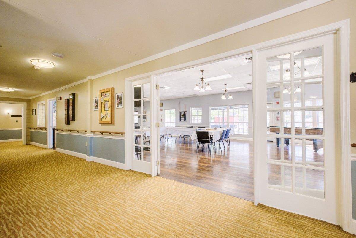 A bright and spacious interior featuring a hallway leading to a dining area with wooden flooring and glass doors.