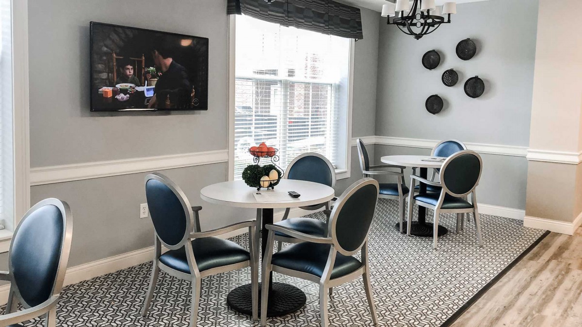 A cozy dining area with round tables, modern chairs, and a television on the wall.