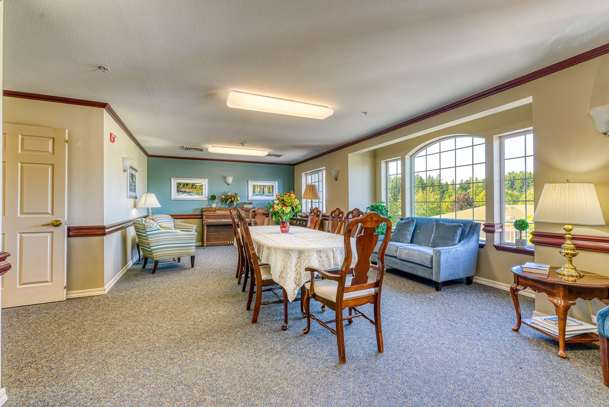 A well-lit dining room with a large table, chairs, and a sofa by the window.