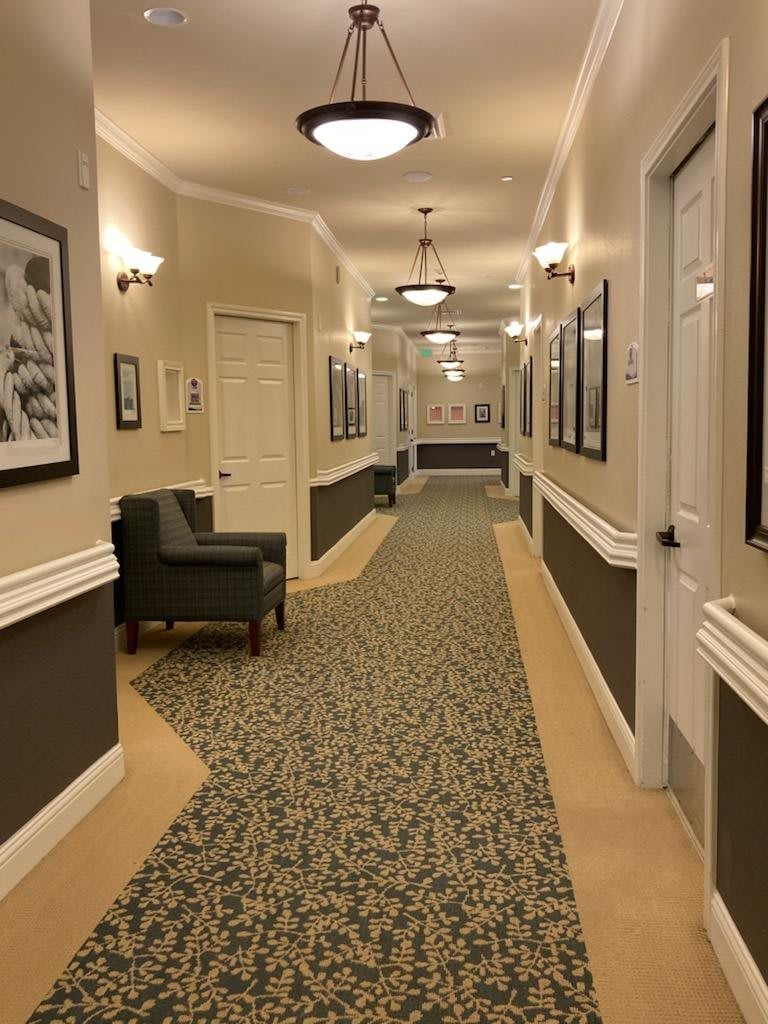 A warmly lit corridor with chairs, artwork on the walls, and patterned carpet.