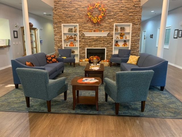 A cozy living room with a fireplace, featuring blue chairs, a coffee table, and decorative shelves.