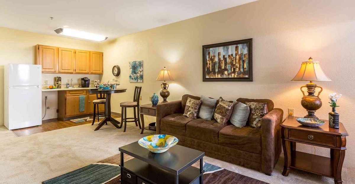 A cozy living room with a brown sofa, coffee table, and dining area, featuring elegant artwork and decorative elements.