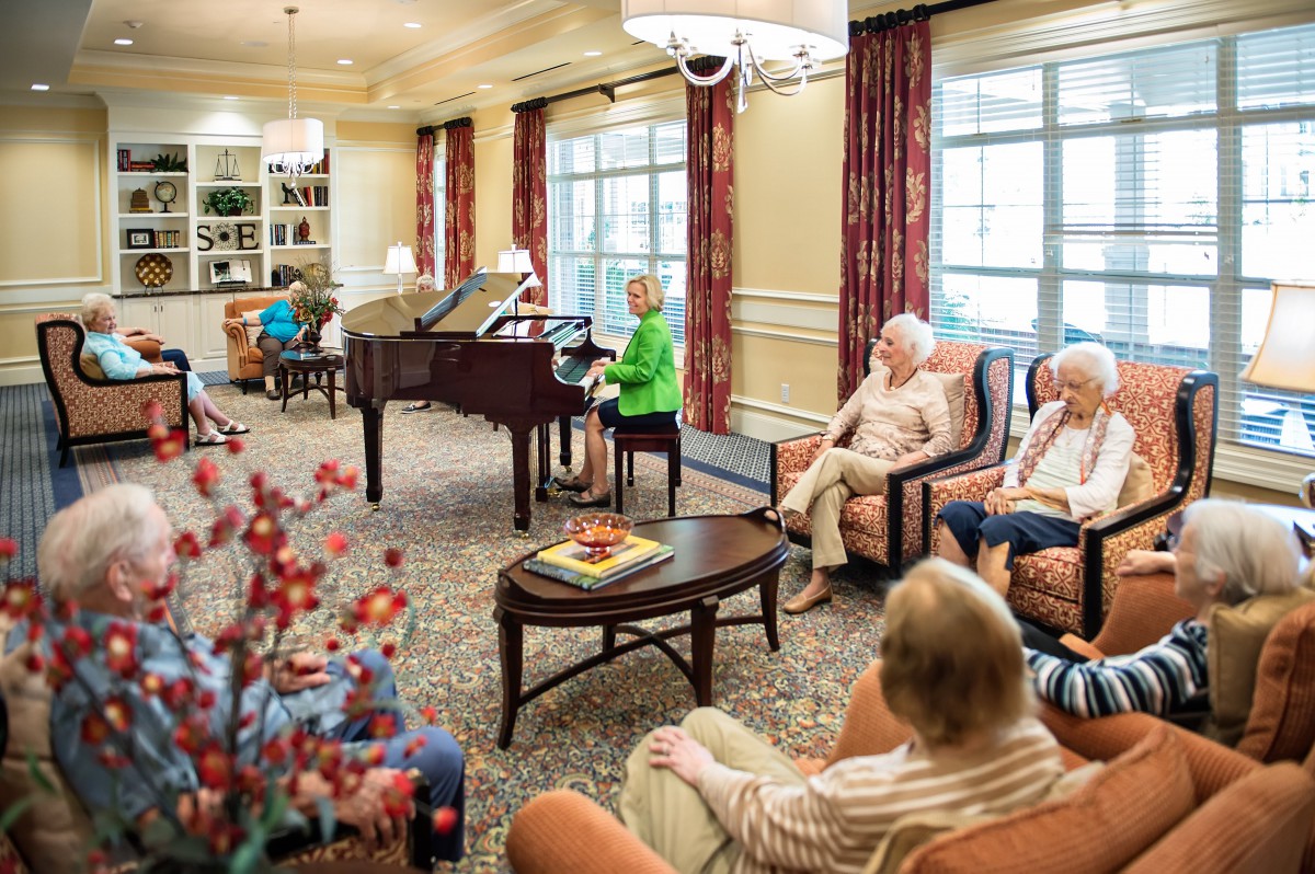 Elderly residents enjoying a social gathering in a comfortable community living room with a piano.