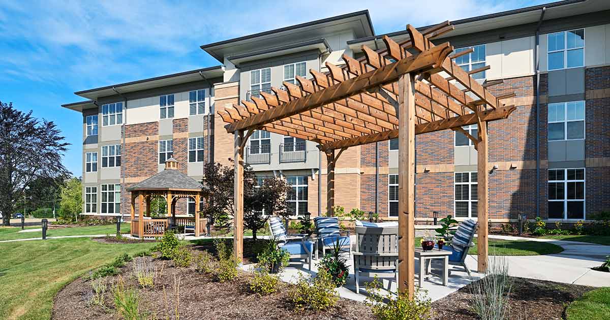 A modern apartment complex features an outdoor patio with a wooden pergola and seating area.