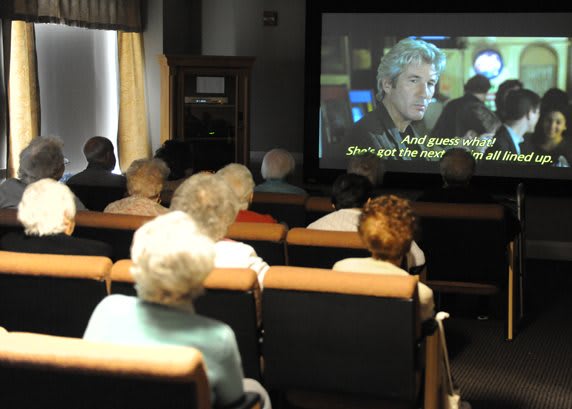 A group of elderly people watching a movie in a small theater.