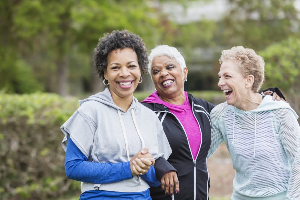 Three women enjoy a happy moment outdoors in a park, smiling and laughing together.