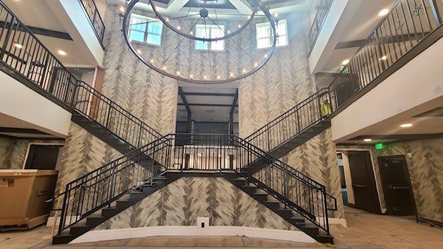 A spacious interior featuring a modern staircase with industrial elements and a large circular chandelier.