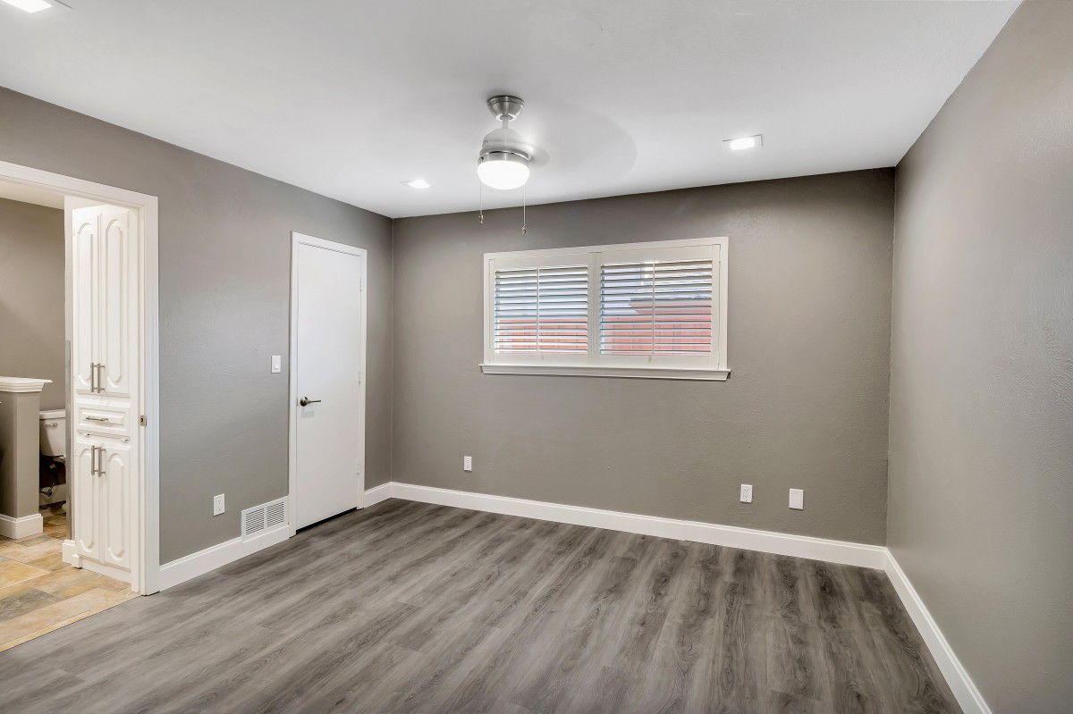 An empty room with gray walls, laminate flooring, a ceiling fan, and a window with blinds.