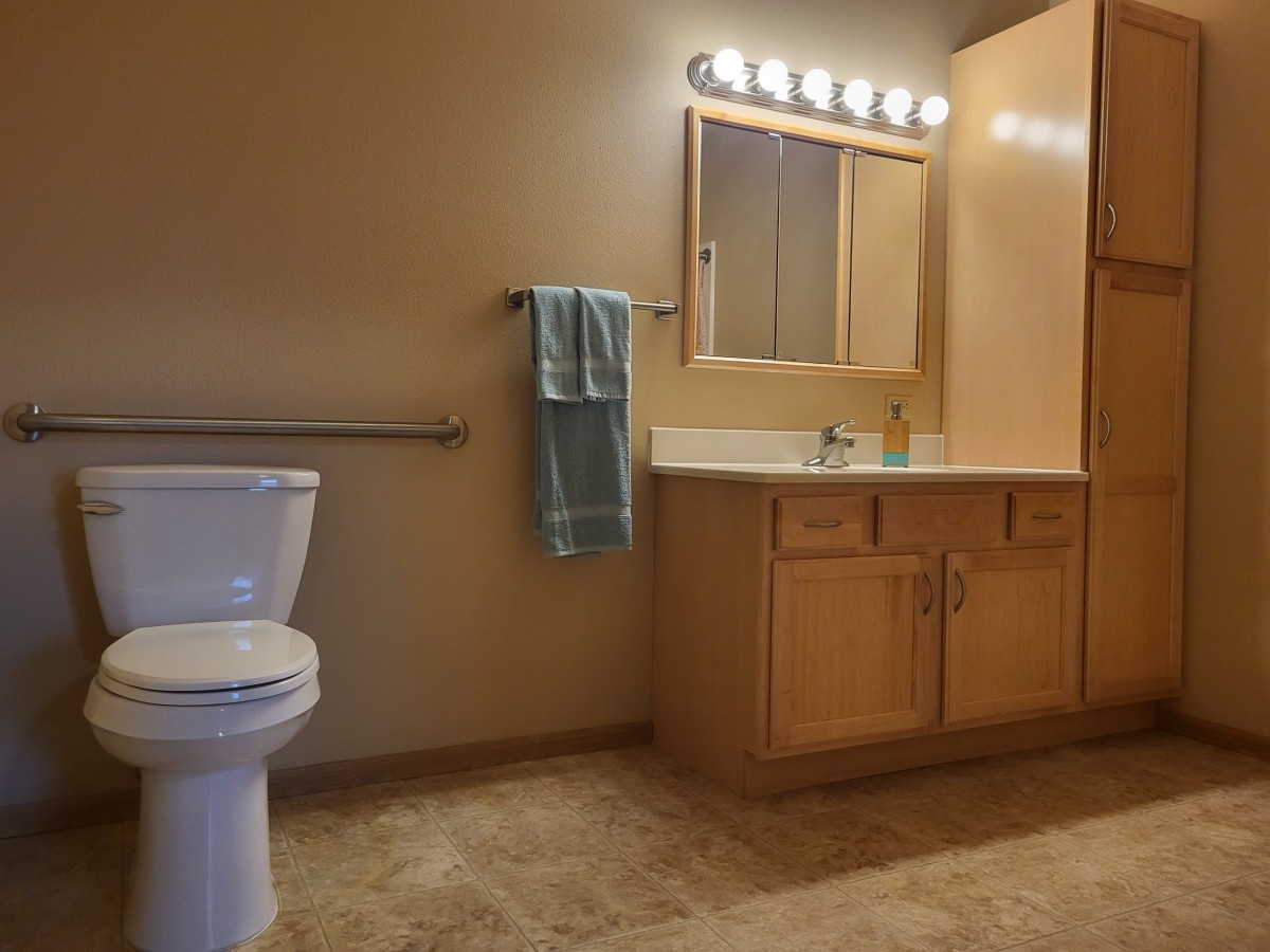 A bathroom with a toilet, sink, and cabinet illuminated by vanity lights.
