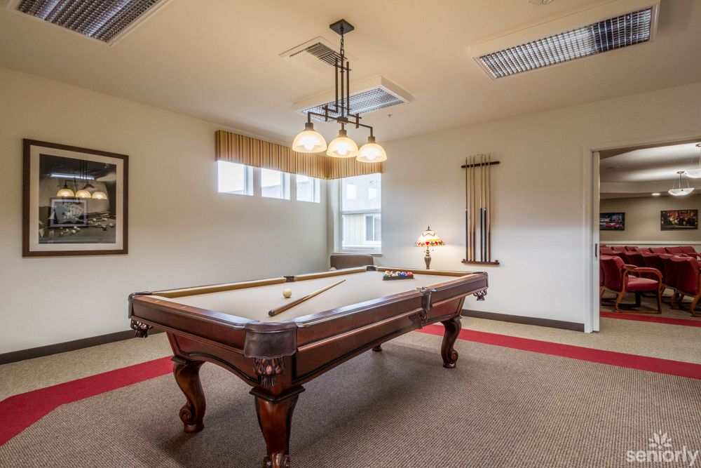 A well-lit game room featuring a billiards table and cue sticks.