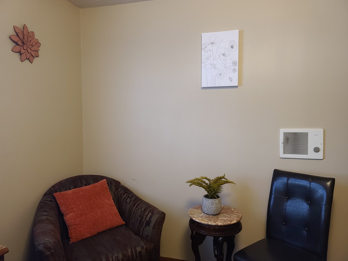 A cozy corner with two chairs, a small plant on a table, and an artwork on the wall.