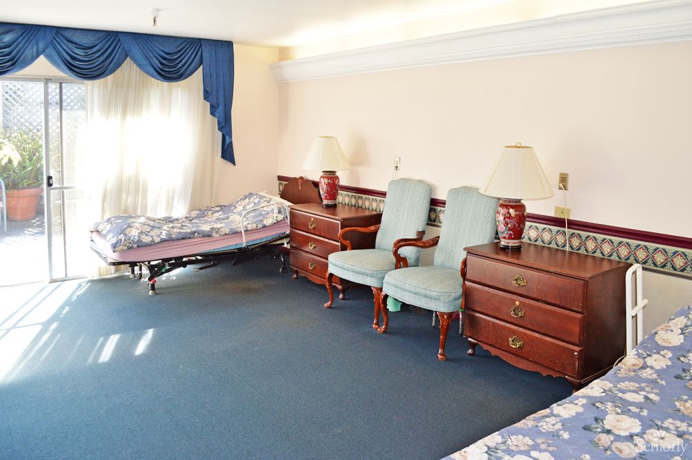 A spacious bedroom with classic furniture, including two chairs, a daybed, and wooden chests of drawers.