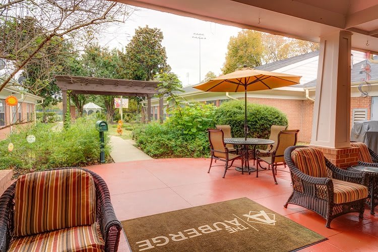 A cozy outdoor patio with table, chairs, and an umbrella surrounded by lush greenery.