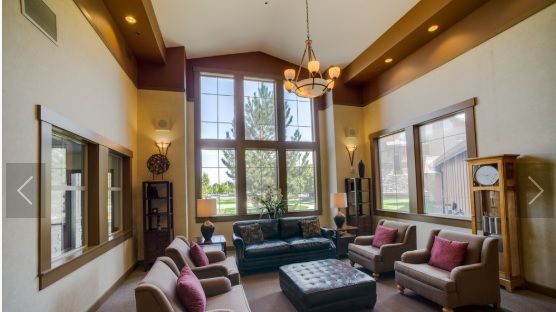 A spacious and elegantly designed living room featuring large windows, comfortable seating, and a central chandelier.