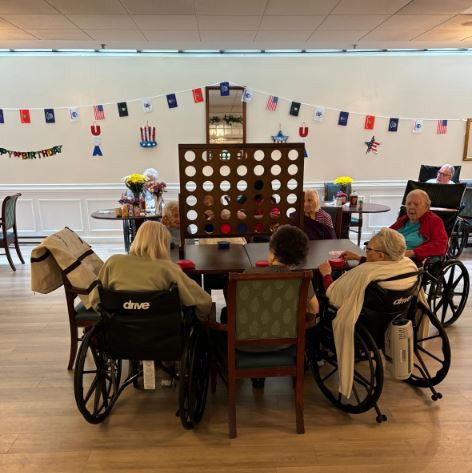 A group of elderly individuals in wheelchairs playing a large Connect Four game indoors.