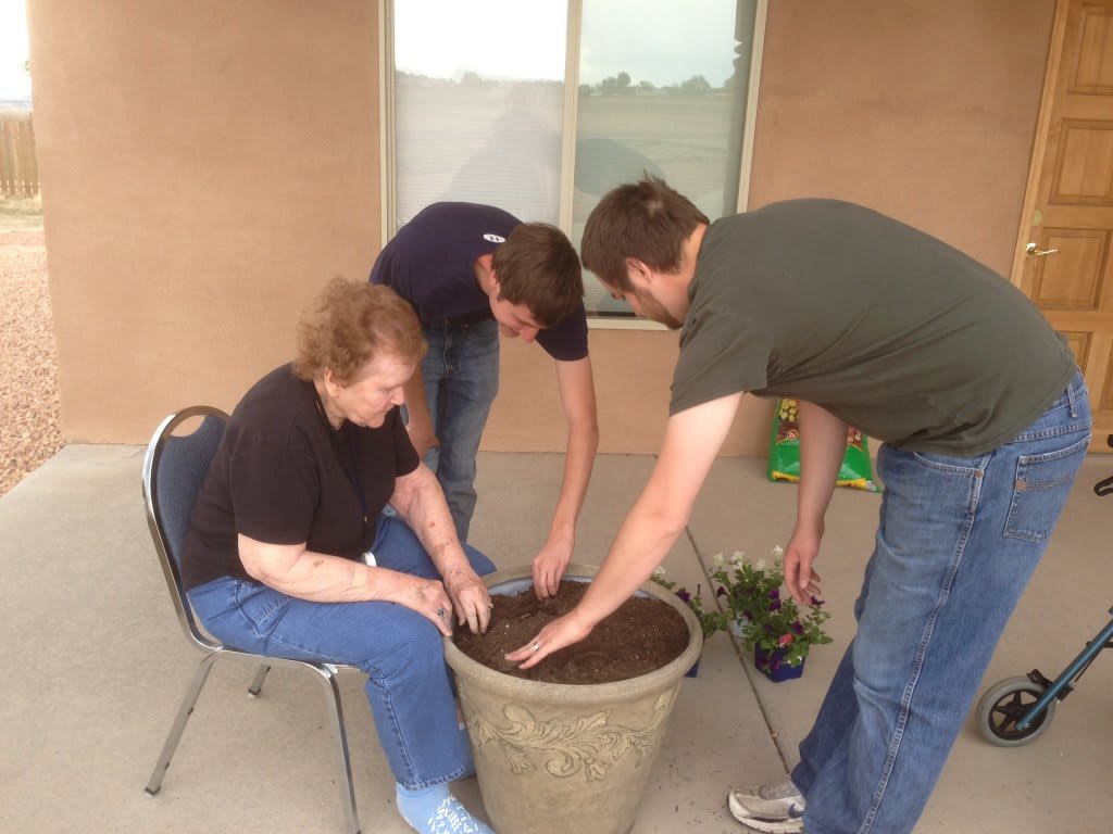A group of people planting in a large pot together on a patio.