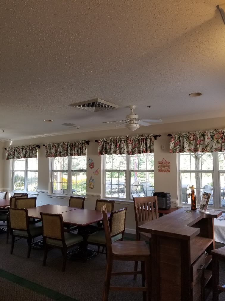 A spacious dining room with multiple tables and chairs, featuring large windows adorned with curtains.