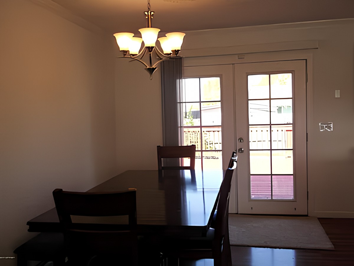 A dining room with a table, chairs, and a chandelier near glass doors leading outside.