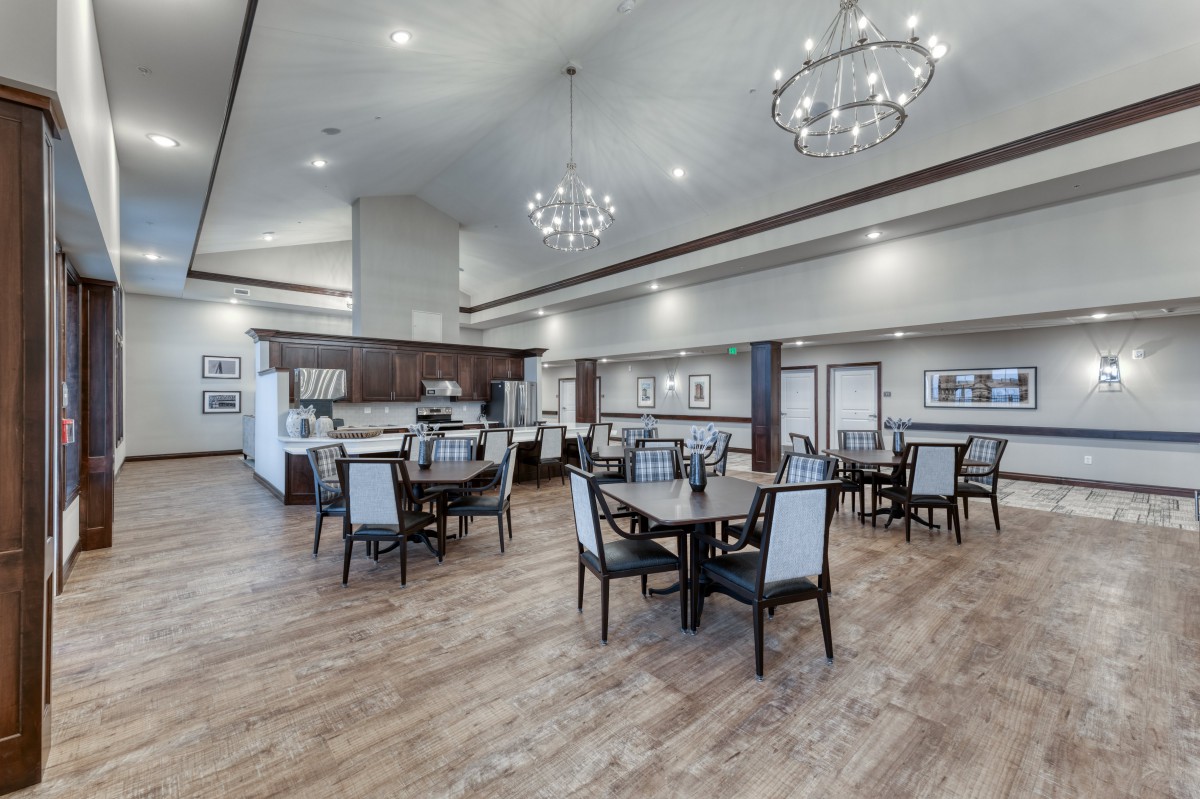 A spacious, elegantly designed dining area featuring modern chandeliers and a comfortable seating arrangement with wood flooring.
