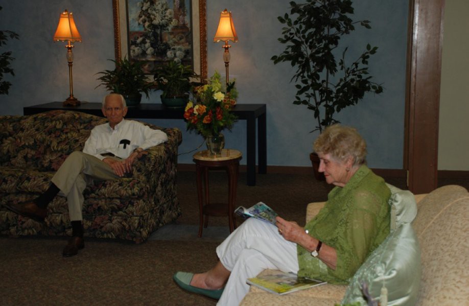 Two elderly people relaxing in a living room, with one reading a book and the other seated comfortably.