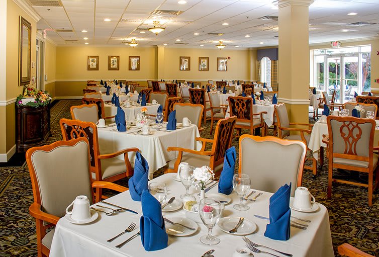 An elegantly set dining room with neatly arranged tables and chairs, featuring blue napkins.