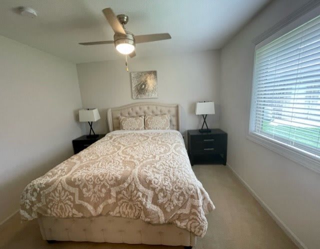 A cozy bedroom featuring a bed with patterned bedding, flanked by nightstands and lamps, and a ceiling fan above.