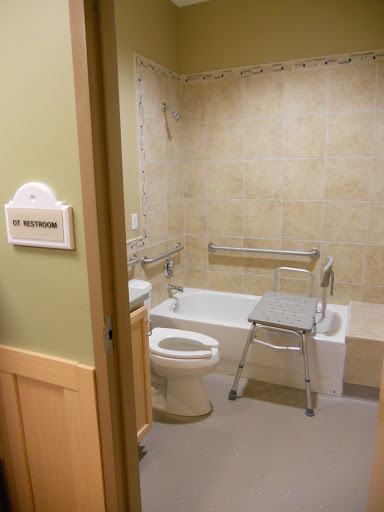 An accessible bathroom featuring a toilet, bathtub with grab bars, and a shower chair.
