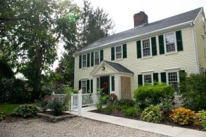 A charming colonial-style house with a manicured garden and a gravel pathway.