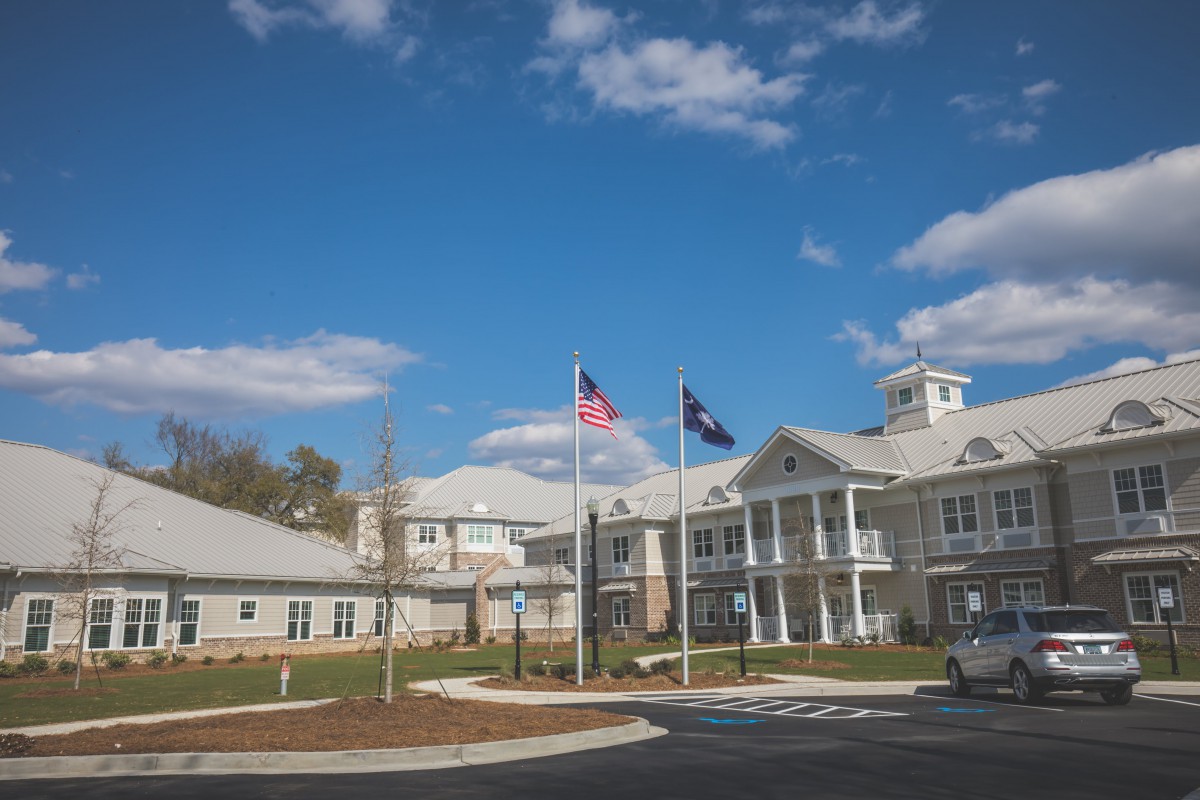 A white building with flags flying in front, set against a blue sky with scattered clouds.