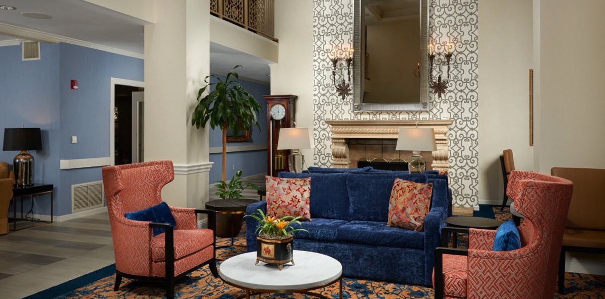 A cozy living room with a blue sofa, patterned throw pillows, and a fireplace featuring an ornate mirror above it.